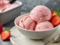 Schüssel mit cremigem Erdbeer-Eis mit Kondensmilch, garniert mit frischen Erdbeeren. Daneben ein Behälter mit Eis.