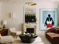 Un dormitorio eclectico con sofá marrón, dos sillones de tweed, mesa de centro de piedra negra, chimenea de mármol y arte abstracto vibrante.