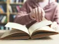 Otwarta księga na stole, w tle regały pełne książek. To początek podróży przez arcydzieła literatury światowej, lista skarbów do odkrycia.
