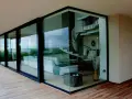 Nowoczesne okno narożne z widokiem na salon ze spiralnymi schodami i taras z drewnianej deski.