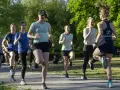 En grupp kvinnor tränar löpning utomhus. De springer i ett parkliknande område, redo att springa 1 km tid.