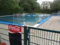 Erfrischung im Monbijou Bad: Wasser 21°C. Menschen schwimmen im blauen Becken, umgeben von Bäumen und einem modernen Gebäude.