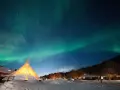 Nocne niebo nad nordkapp camping rozświetla zorza polarna. W dole ośnieżony teren i oświetlony namiot.