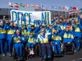 Ukraińska drużyna paraolimpijska z podniesionymi pięściami przed transparentem "Peace for All". Nadzieja na pokój na igrzyskach paraolimpijskich 2026.