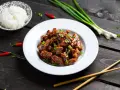 Pyszny kurczak luc lac w sosie, posypany sezamem i szczypiorkiem, obok ryż i papryczki chili.