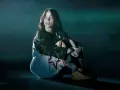 Billie Eilish w ciemnym pomieszczeniu, siedzi w pozie zamyślenia. Jej stylizacja nawiązuje do estetyki jej albumu.