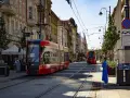 Czerwony tramwaj na ulicy w Katowicach. W tle kamienice i inny tramwaj. To widok na katowice stare miasto.