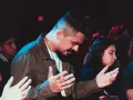 A man with his hands raised in prayer, part of a congregation following the order of prayer.