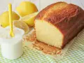 Bizcocho de yogur casero, dorado y esponjoso, acompañado de limones frescos y un vasito de yogur.