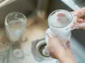 Händer tvättar glas med skum i diskho för att glaspest ta bort.