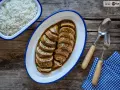 Calamares rellenos en salsa, servidos en una bandeja ovalada junto a un bol de arroz blanco. Cubiertos con cebollino picado.