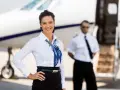 Assistente di volo sorridente accanto a un jet privato. Scopri come diventare assistente di volo e iniziare la tua carriera nel cielo.