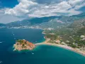 Sveti Stefan, Czarnogóra czy warto? Widok z lotu ptaka na malowniczą wyspę połączoną z lądem, turkusowe morze i górzyste wybrzeże.