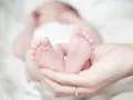 Delikatne stópki noworodka w dłoniach rodzica. Zastanawiasz się, ile ml powinien jeść noworodek?
