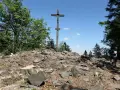 Kamienisty szczyt z drewnianym krzyżem, otoczony drzewami. Idealne miejsce na wędrówkę po górach świętokrzyskich szlaki.