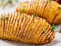 Deux pommes de terre hasselback dorées et croustillantes, garnies d'herbes fraîches. Un délice visuel et gustatif.