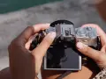 Dłonie trzymają srebrny aparat Fujifilm XT50, obracając pokrętło trybów filmowych.