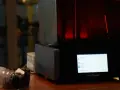 A HeyGears resin printer with a red interior light. Beside it, a camera lens. This setup hints at the process of how long to cure resin prints.