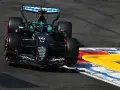 El coche de F1 Aston Martin número 18 se inclina en una curva, con sus neumáticos rozando la línea de la pista.