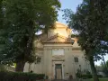A serene church facade at Tre Fontane, Rome, bathed in golden light, framed by lush green trees.