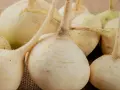 Grupka świeżych, białych rzep na płóciennym tle. Ich korzenie i łodyżki dodają naturalnego uroku.