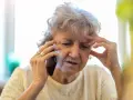 Zmartwiona starsza pani rozmawia przez telefon, szukając informacji, jak napisać rezygnację z sanatorium do NFZ.