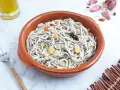 Un cuenco de barro con gulas al ajillo, adornado con láminas de ajo dorado y un chile seco.