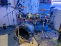 Der **Aufbau Schlagzeug** ist bereit für den nächsten Gig. Glänzende Trommeln und Becken stehen auf stabilen Stativen, beleuchtet von blauem Licht.