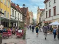 Tłum ludzi spaceruje brukowaną ulicą w Wilnie, siedząc przy stolikach restauracyjnych. Czy wyjazd na Litwę jest bezpieczny? Wygląda na to, że tak!
