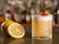 Orzeźwiający drink z amaretto, ozdobiony wiśnią i cytryną, stoi obok świeżych cytryn na barze.