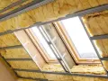 Wełna mineralna w trakcie montażu na poddaszu, widoczne profile stalowe i okna dachowe.
