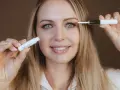 Frau mit blauen Augen trägt ein Serum auf ihre Wimpern auf, um sie wachsen zu lassen.