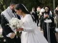 Panna młoda w białej sukni z welonem trzyma bukiet, pan młody w garniturze z szalem.