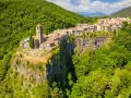 Un borgo medievale, Castellfollit de la Roca, aggrappato a una scogliera basaltica, circondato da lussureggianti foreste verdi.