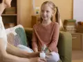 Rozmowa psychologa z rodzicem o zdrowiu dziecka. Dziewczynka z piegami słucha uważnie.