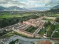 Vasta Certosa di Padula, un complesso monastico imponente con cortili verdi, circondato da alberi e montagne sullo sfondo.