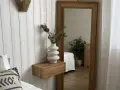 Estantería flotante de madera con jarrón blanco y ramas secas, ideal para ideas para decorar rincones pequeños. Reflejo de planta y cama en espejo grande.