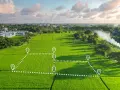 Wyznaczona liniaami i pinezkami działka ewidencyjna na tle zielonych pól ryżowych i zabudowań.