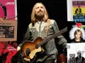 Tom Petty mit Bass, umgeben von Albumcovern wie "Full Moon Fever" und "Wildflowers". Ein Blick auf die Musikikone.