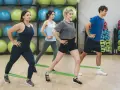 Grupa osób ćwiczy z gumami oporowymi. W tle widać piłki gimnastyczne. To świetny abt trening!