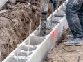 Beton wylewany do szalunku z bloczków betonowych, zbrojenie wystaje. Budowa fundamentów w toku.
