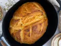 Ein goldbraunes Brot mit knuspriger Kruste liegt in einem Gusseisentopf. Dieses Brot kommt nicht aus dem Topf, sondern wurde darin gebacken.