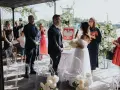 Uroczyste wesele w ogrodzie. Para młoda stoi przed urzędniczką, goście obserwują ceremonię.