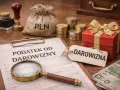 Dokument "Podatek od darowizny", lupa, worek z napisem PLN, monety, czerwone pudełko z kokardą i banknoty.