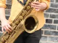 Hände spielen ein goldenes Saxophon. Obwohl es aus Metall ist, ist das Saxophon ein Holzblasinstrument, da der Ton durch ein Rohrblatt erzeugt wird.