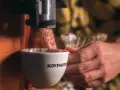 Mielona kawa spada do filiżanki z napisem "Kofimatik". Idealna baza do kawy z likierem kawowym Baileys.