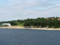 Słoneczny dzień nad jeziorem Chańcza. Piękna plaża, las i kilka domków w tle. Ludzie odpoczywają i kąpią się.