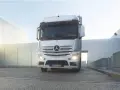 Biały Mercedes Actros MP4 z włączonymi światłami stoi przed nowoczesnym budynkiem.