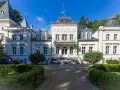 Elegancki pałac w Nosowie z wieżyczkami i ozdobnym balkonem, otoczony zielenią.