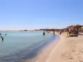 Słoneczna plaża Elafonisi z turkusową wodą i piaskiem, pełna ludzi kąpiących się i odpoczywających pod parasolami.